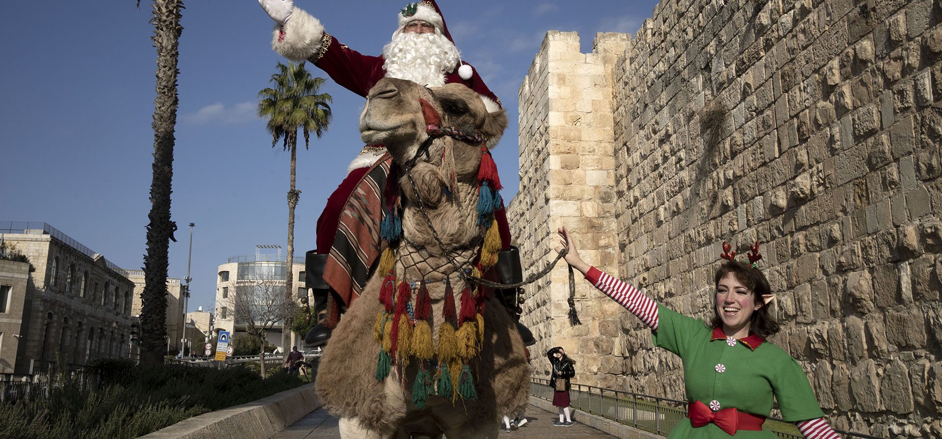 Un hombre, vestido como Papá Noel, monta un camello llamado en la Ciudad Vieja de Jerusalén, antes de las vacaciones de Navidad, el jueves 22 de diciembre de 2022. (Foto AP/Maya Alleruzzo)