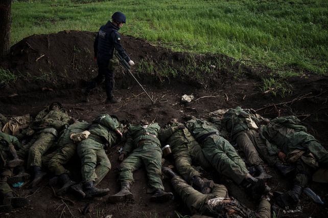 Un soldado ucraniano del equipo de desminado camina al lado de los cuerpos de efectivos rusos abandonados en Vilkhivka.
