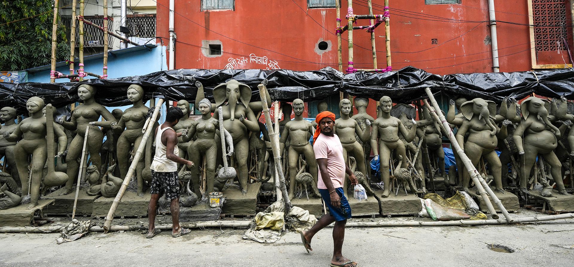 Un hombre pasa junto a un artesano que trabaja en un ídolo de arcilla de la diosa hindú Durga en su estudio temporal al borde de la carretera antes del festival Durga Puja en Kumortuli, el lugar de los alfareros, en Calcuta, India. El festival de cinco días conmemora el asesinato de un rey demonio por la diosa Durga, que marca el triunfo del bien sobre el mal.