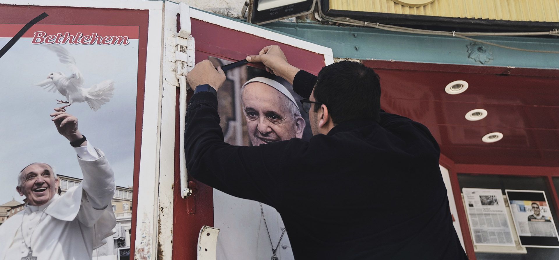 El dueño de una tienda limpia y coloca una cinta negra sobre una foto del difunto Papa Francisco tras la noticia de su fallecimiento a los 88 años, en Belén, Cisjordania, el lunes 21 de abril de 2025. (Foto AP/Mahmoud Illean) El dueño de una tienda limpia y coloca una cinta negra sobre una foto del difunto Papa Francisco tras la noticia de su fallecimiento a los 88 años, en Belén, Cisjordania, el lunes 21 de abril de 2025. (Foto AP/Mahmoud Illean)