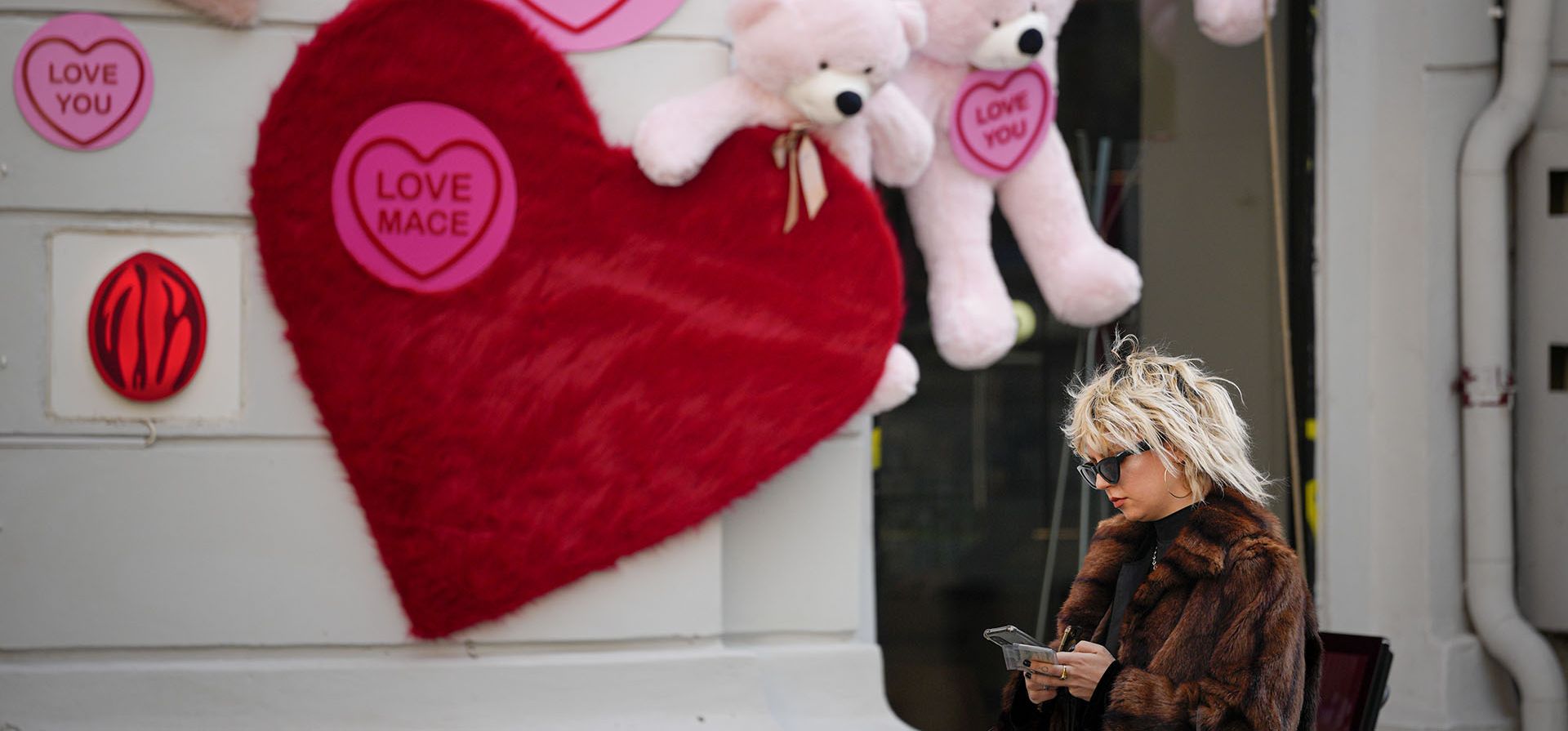 Una mujer revisa su teléfono junto a una tienda decorada con ositos de peluche y recortes en forma de corazón en Bucarest, Rumania, el martes 14 de febrero de 2023. Nunca antes de la caída del gobierno comunista en Rumania en 1989, el Día de San Valentín se volvió cada vez más popular. en los años siguientes y ahora es ampliamente adoptado por los jóvenes rumanos. (Foto AP/Andreea Alexandru)