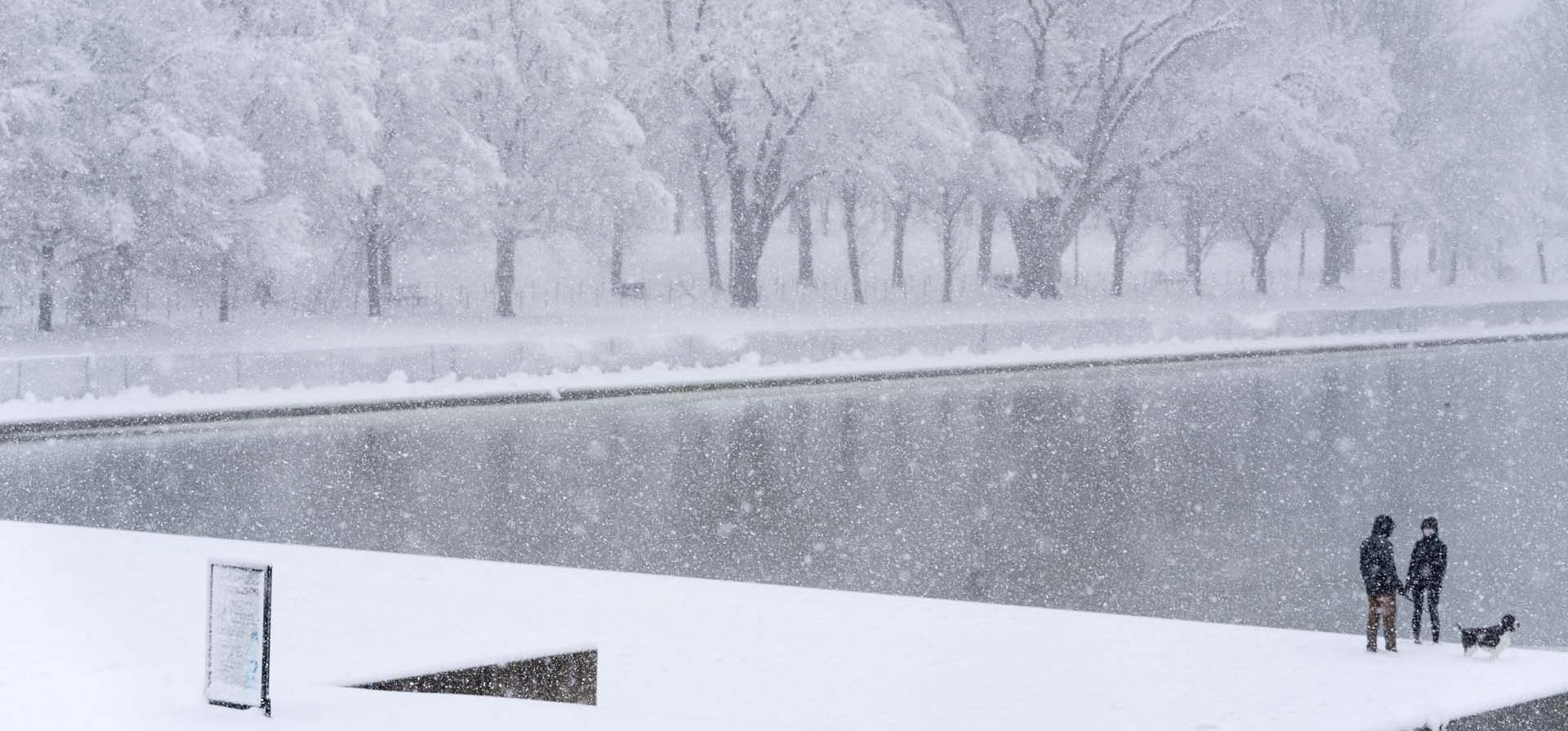 La gente pasea a su perro cerca de la Piscina Reflectante del Monumento a Lincoln mientras cae la nieve en Washington.