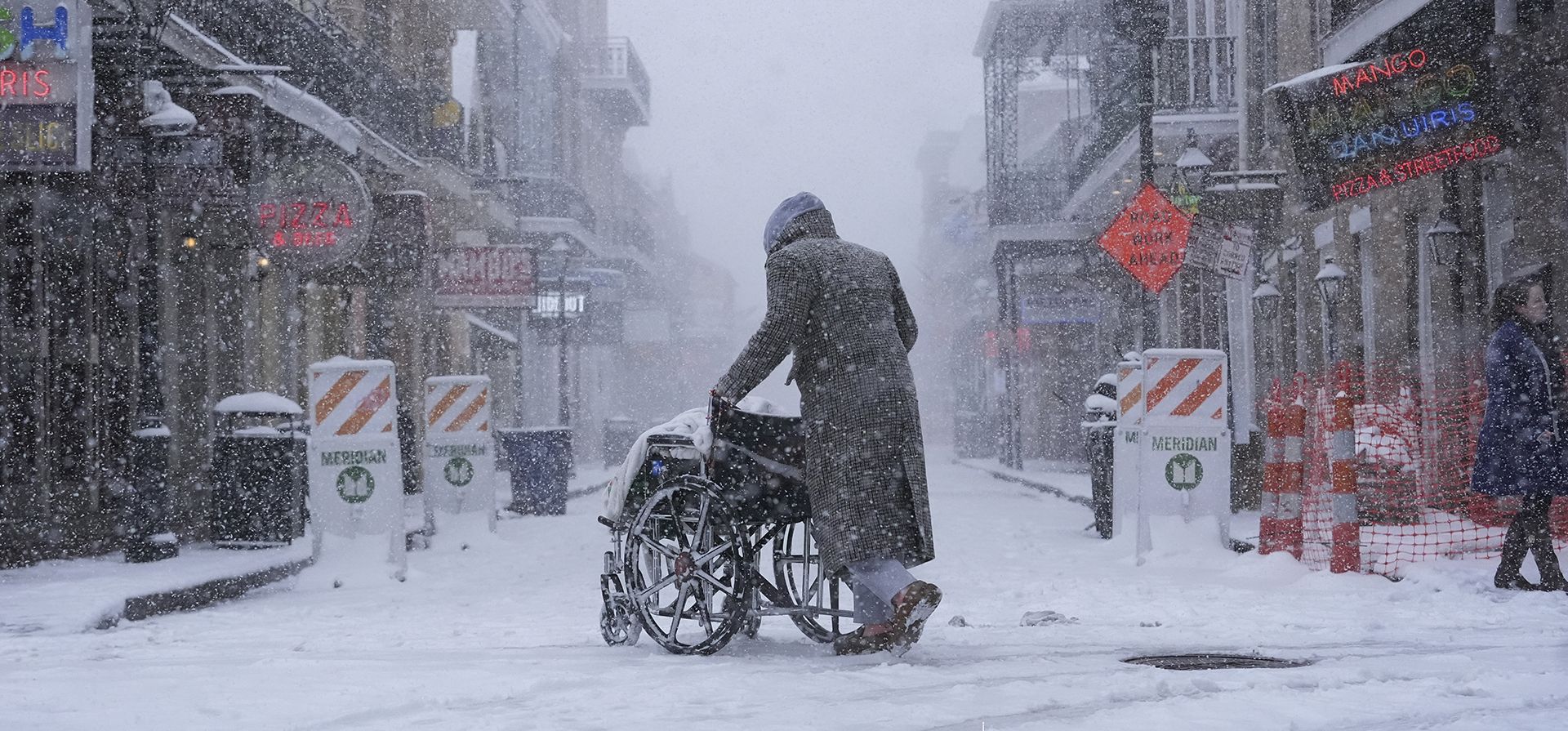 Una persona empuja una silla de ruedas por la calle Bourbon mientras cae nieve en el Barrio Francés de Nueva Orleans, el martes 21 de enero de 2025. (Foto AP/Gerald Herbert)