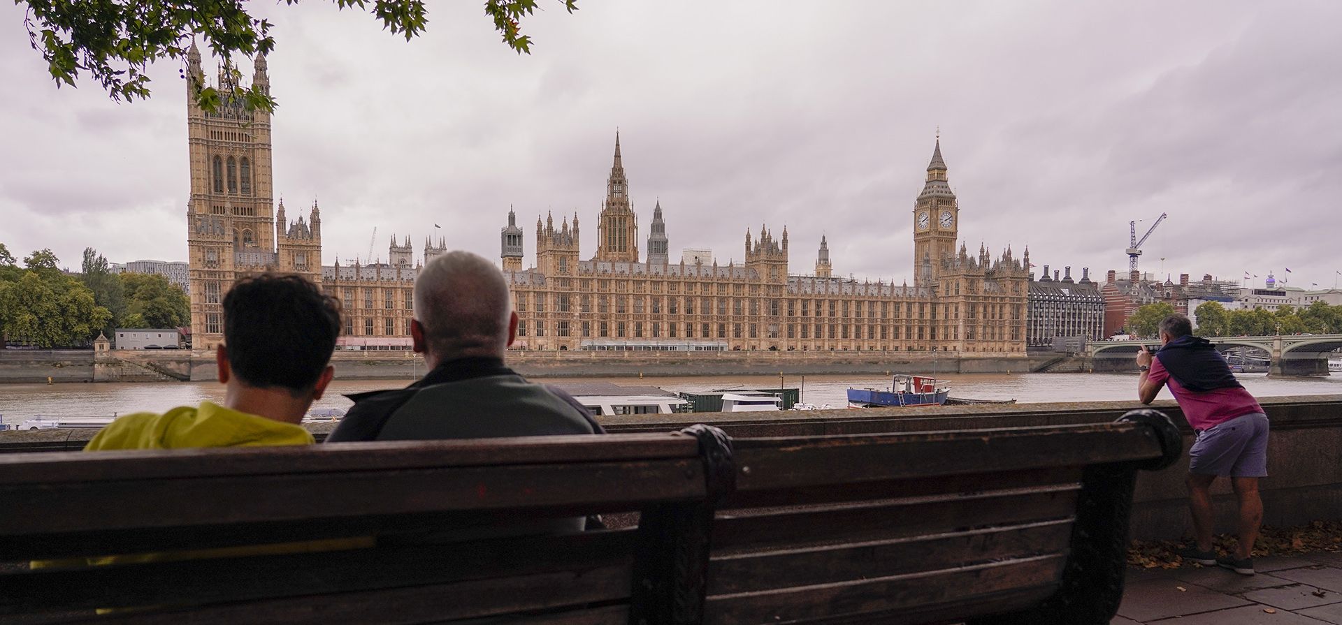 La gente descansa en un banco mientras mira el Palacio de Westminster, en la orilla sur del río Támesis, en Londres, el martes 4 de octubre de 2022. La investigación pública sobre la respuesta del Reino Unido a la pandemia de covid-19 y su impacto, comenzó en Londres.