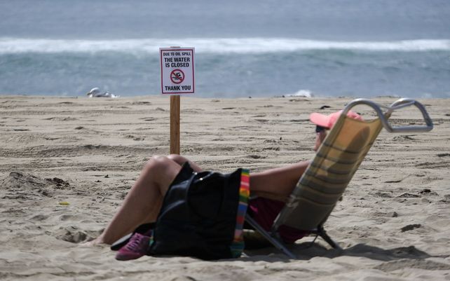 Un bañista descansa frente a un letrero de advertencia después de un derrame de petróleo en Huntington Beach, California. Un gran derrame de petróleo frente a la costa del sur de California contaminó playas y mató a la vida silvestre.
