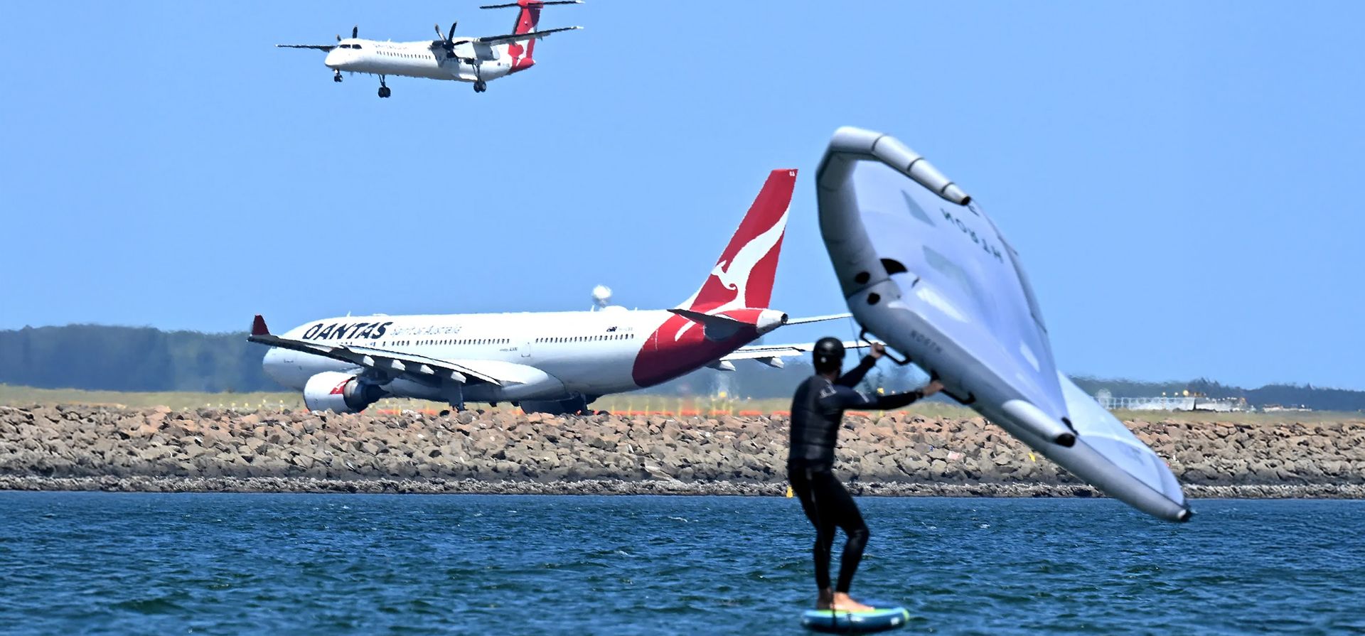 Un surfista se desliza por el agua mientras un avión de Qantas espera despegar en el aeropuerto internacional de Sídney, Sídney, Australia. Fotografía: Saeed Khan/AFP/Getty Un surfista se desliza por el agua mientras un avión de Qantas espera despegar en el aeropuerto internacional de Sídney, Sídney, Australia. Fotografía: Saeed Khan/AFP/Getty