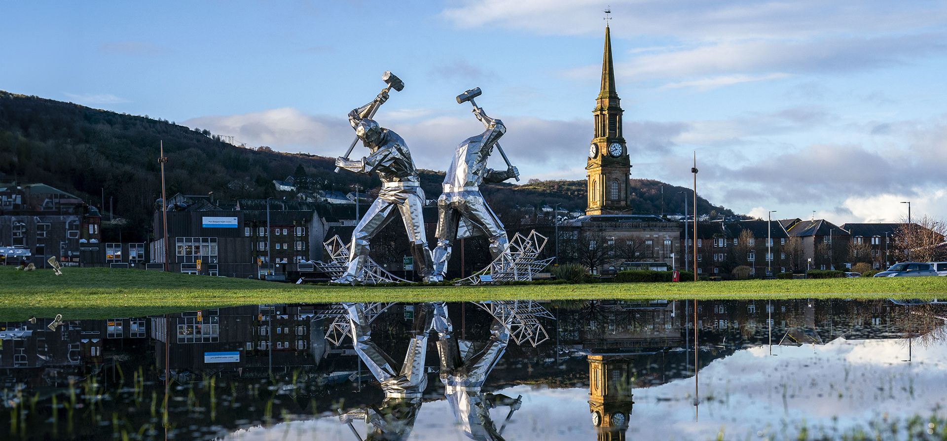 La escultura de los constructores navales de Port Glasgow en Coronation Park, Inverclyde, se refleja en grandes charcos después de fuertes lluvias, en Port Glasgow, Escocia, el viernes 5 de enero de 2023. El impacto de las aguas superficiales y las inundaciones de los ríos seguirá siendo "significativo" en todas partes del país tras las inundaciones por las lluvias. (Jane Barlow/PA vía AP)