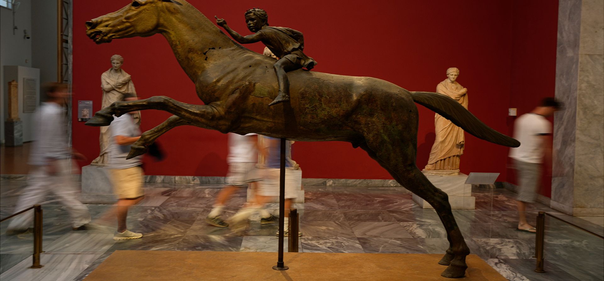 Turistas pasan junto a la estatua de bronce de un joven jinete a caballo, conocida como el Jinete de Artemision, que data del año 140 a. C., en el Museo Arqueológico Nacional de Atenas, Grecia, el miércoles 24 de junio de 2026. (Foto AP/Thanassis Stavrakis) Turistas pasan junto a la estatua de bronce de un joven jinete a caballo, conocida como el Jinete de Artemision, que data del año 140 a. C., en el Museo Arqueológico Nacional de Atenas, Grecia, el miércoles 24 de junio de 2026. (Foto AP/Thanassis Stavrakis)