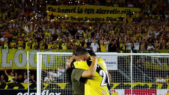 El futbolista y su esposa se abrazan con la bandera de apoyo de los hinchas del equipo de fondo.&nbsp;