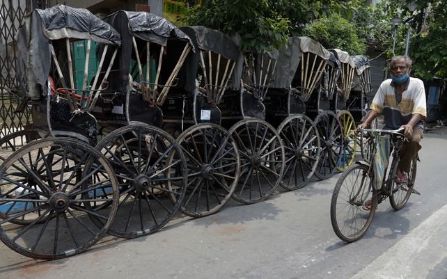 Un hombre pedalea junto a rickshaws estacionados durante el relajamiento de restricciones debido a la pandemia de coronavirus en Calcuta