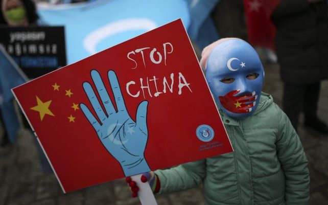 Un niño con mascara de la comunidad uigur que vive en Turquía sostiene una pancarta anti-China durante una protesta contra la visita del ministro de Relaciones Exteriores de China, Wang Yi, a Turquía, en Estambul.