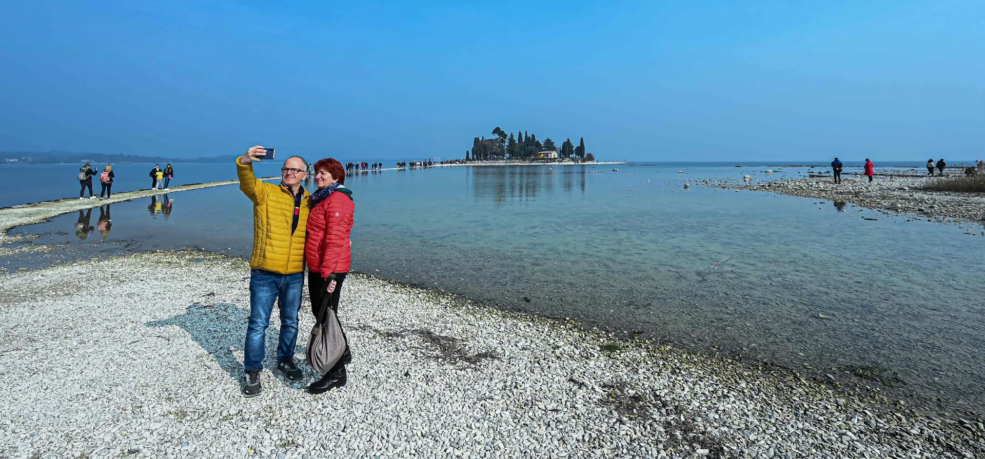 La gente se toma una selfie frente a la pequeña isla de San Biagio, frente a Manerba en el lago de Garda, donde el nivel del agua cayó a su nivel más bajo en 30 años durante los meses de invierno debido a la falta de nieve en los picos de las montañas circundantes, la ausencia de lluvia y las temperaturas suaves, Lago de Garda, Italia. Fotografía: Piero Cruciatti/AFP/Getty Images