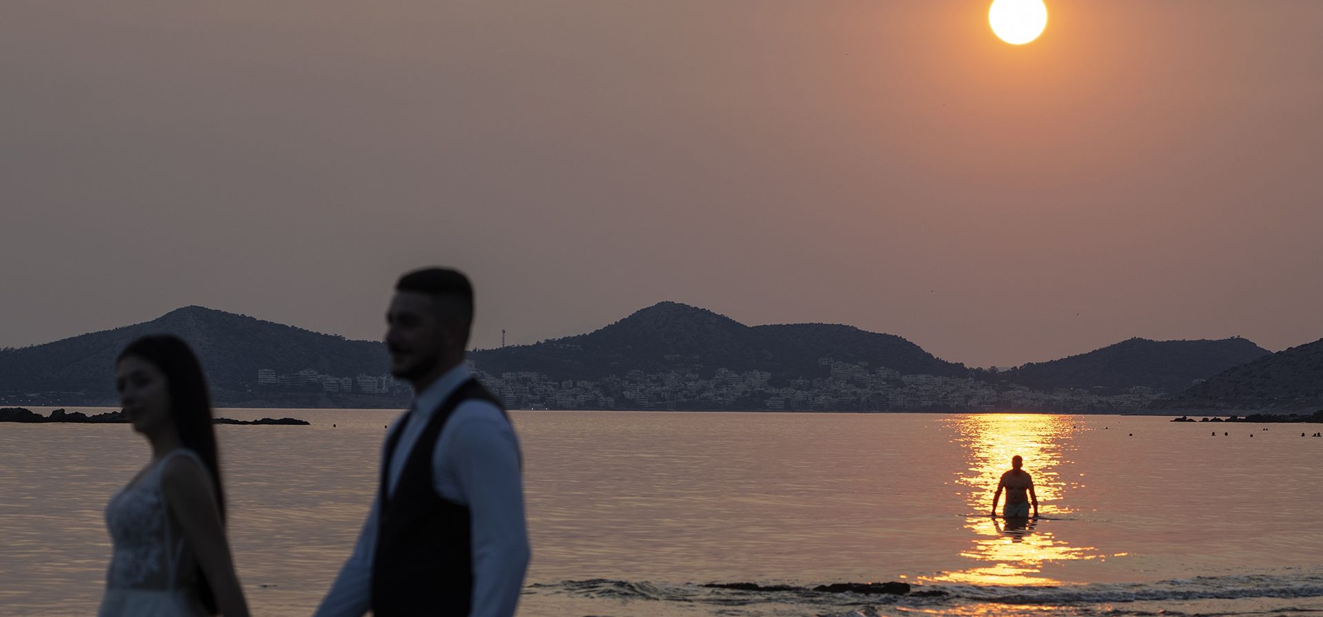 Una pareja de recién casados posa para las fotos durante la puesta de sol mientras un hombre se sumerge en el agua en Lagonisi, al sureste de Atenas, el miércoles 12 de julio de 2023. (Foto AP/Petros Giannakouris) Una pareja de recién casados posa para las fotos durante la puesta de sol mientras un hombre se sumerge en el agua en Lagonisi, al sureste de Atenas, el miércoles 12 de julio de 2023. (Foto AP/Petros Giannakouris)