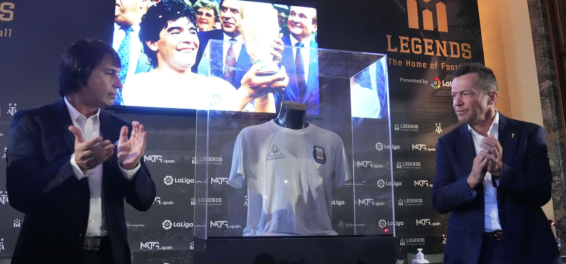 El ex futbolista alemán Lothar Matthaus, y el coleccionista argentino y presidente del museo del fútbol Leyendas Marcelo Ordas, aplauden al develar la camiseta que usó Diego Armando Maradona en la final del Mundial de México 1986, durante un acto en la Embajada Argentina en Madrid, España, el jueves 25 de agosto de 2022. La camiseta fue entregada a Matthaus, luego de que intercambiara camisetas con Maradona al final del partido final. Matthaus ha donado la camiseta al museo del fútbol Legends en Madrid.