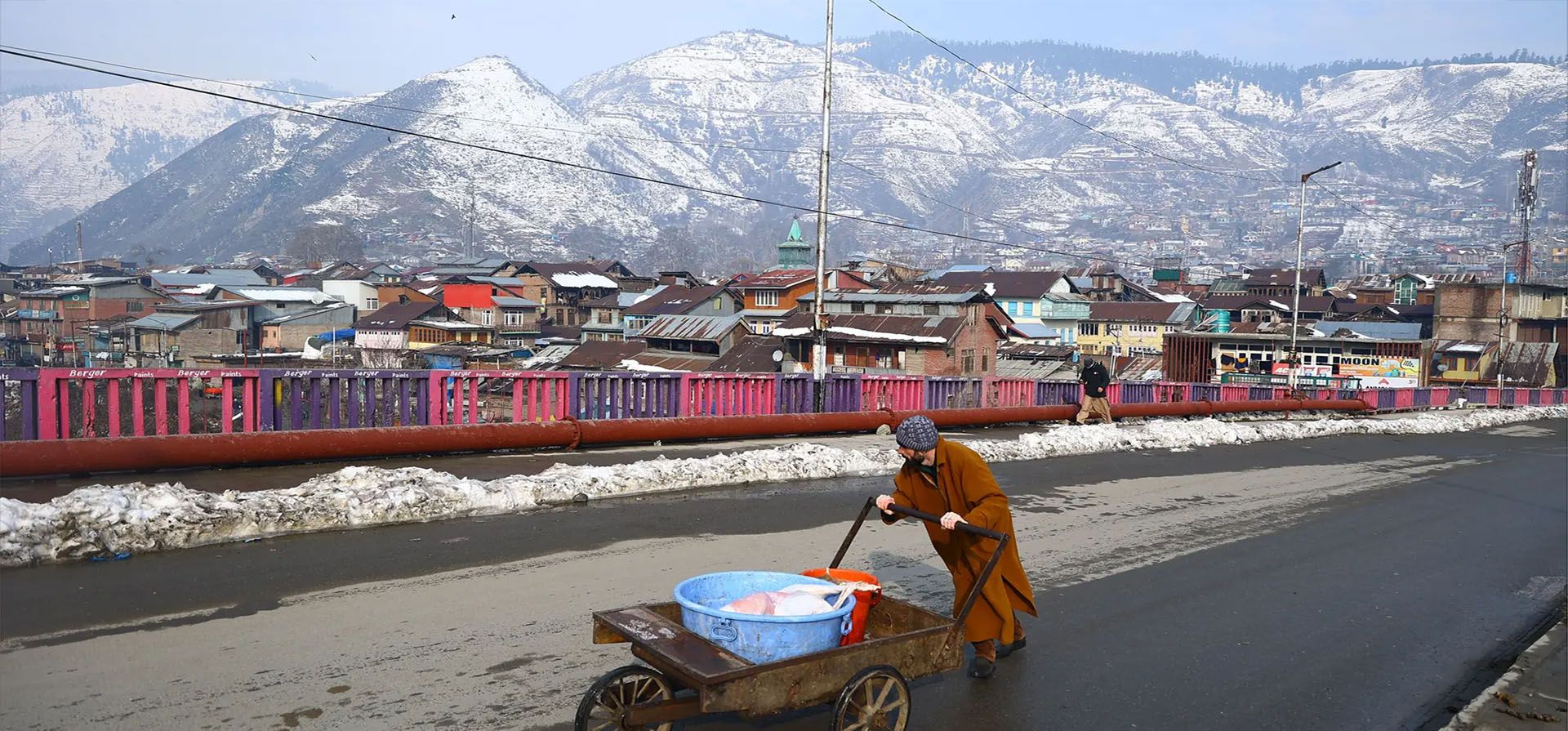 Un hombre empuja un carro frente a montañas cubiertas de nieve en un día frío en Cachemira. Fotografía: Nasir Kachroo/NurPhoto/Shutterstock