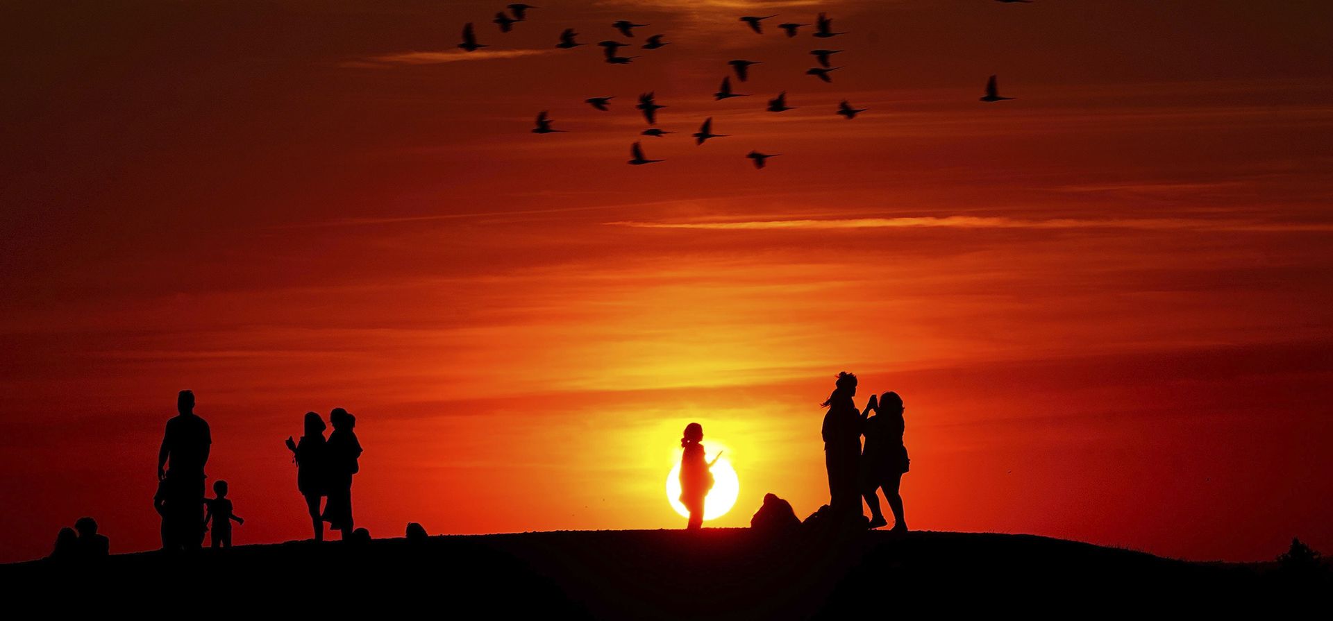 Grupos de personas ven la puesta de sol desde una colina en Ealing, al oeste de Londres, el martes 9 de agosto de 2022, mientras continúa un verano de prohibiciones de riegos, lavado de autos y advertencias de incendios, con una alerta de salud por calor en gran parte del país.