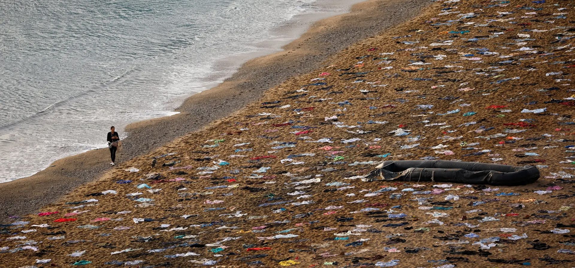Una mujer camina cerca de la ropa que yace en la playa de Sant Sebastià mientras la ONG Open Arms simula la escena de un naufragio para conmemorar a las personas que murieron en el mar Mediterráneo en 2023 mientras intentaban llegar a Europa, Barcelona, España. Fotografía: Albert Gea/Reuters Una mujer camina cerca de la ropa que yace en la playa de Sant Sebastià mientras la ONG Open Arms simula la escena de un naufragio para conmemorar a las personas que murieron en el mar Mediterráneo en 2023 mientras intentaban llegar a Europa, Barcelona, España. Fotografía: Albert Gea/Reuters