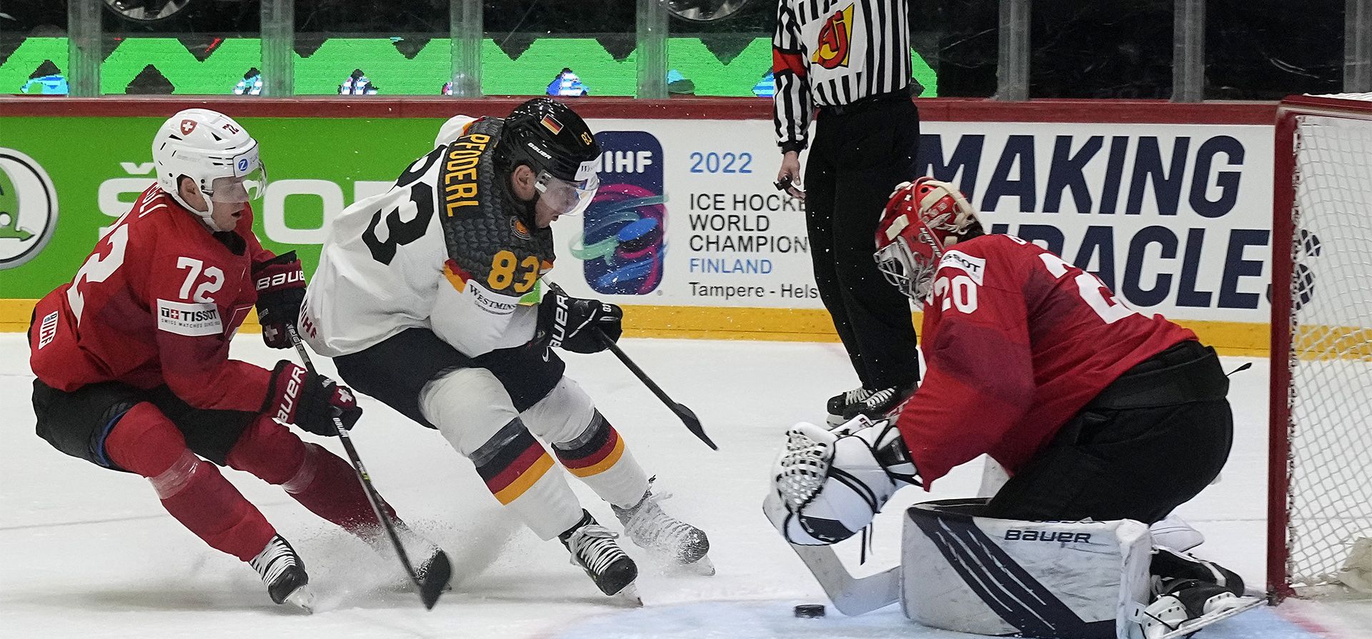 El arquero suizo Reto Berra es desafiado por el alemán Leonhard Pfoderl durante el partido del Campeonato Mundial de Hockey del grupo A entre Alemania y Suiza en Helsinki, Finlandia, el martes 24 de mayo de 2022.