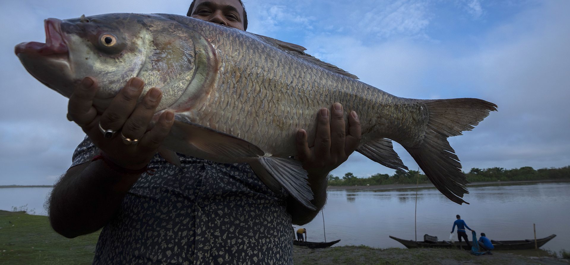 Un hombre muestra un pescado después de comprarlo en un mercado mayorista cerca del río Janji en el alto Assam, al este de Guwahati, India, el lunes 26 de septiembre de 2022.