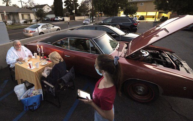 Una camarera atiende a dos comensales en el estacionamiento del restaurante italiano Vitello, en Los Ángeles. Los clientes traen sus propias mesas e incluso sus vajillas para disfrutar de una comida al aire libre.