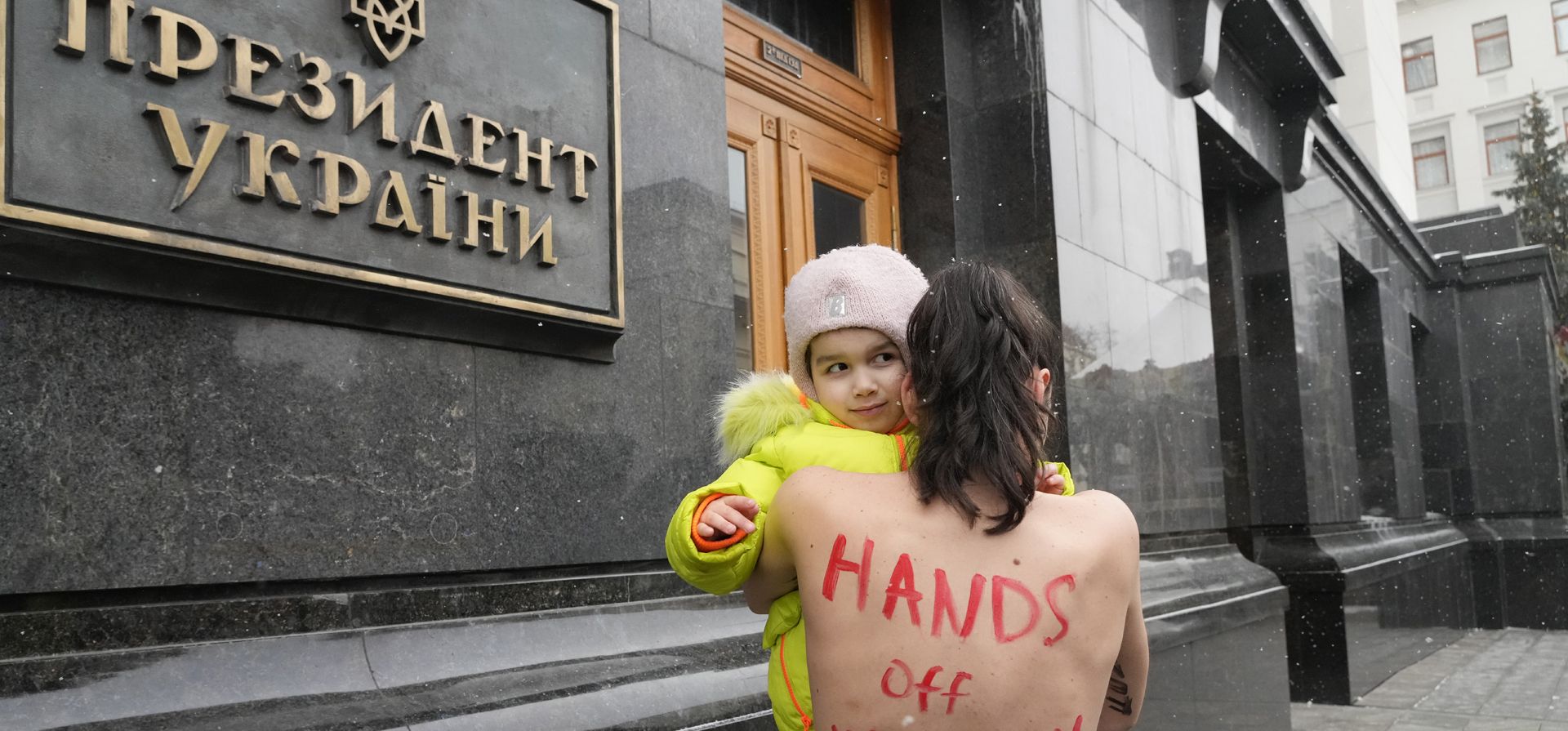 Una activista feminista en topless de FEMEN protesta con su hija frente a la oficina del presidente de Ucrania en Kiev, Ucrania, el jueves 27 de enero de 2022, contra el proyecto gubernamental de registro militar para mujeres.