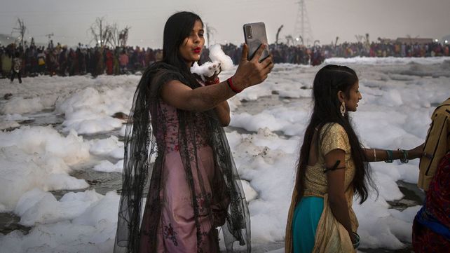 Una devota hindú se toma una selfie mientras sostiene un puñado de espuma química que recogió del río Yamuna durante el festival Chhath Puja en Nueva Delhi, India, el miércoles 10 de noviembre de 2021. Un vasto tramo de uno de los ríos más sagrados de la India, el Yamuna, es cubierto con espuma tóxica, causada en parte por los altos contaminantes vertidos por las industrias que rodean la capital, Nueva Delhi