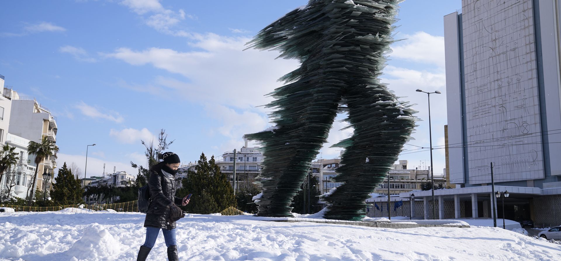 Una mujer pasa junto a un corredor, esculpido por Kostas Varotsos, después de una tormenta de nieve, en Atenas, el martes 25 de enero de 2022. Una tormenta de nieve de rara gravedad interrumpió el tráfico aéreo y por carretera el lunes en la capital griega de Atenas.