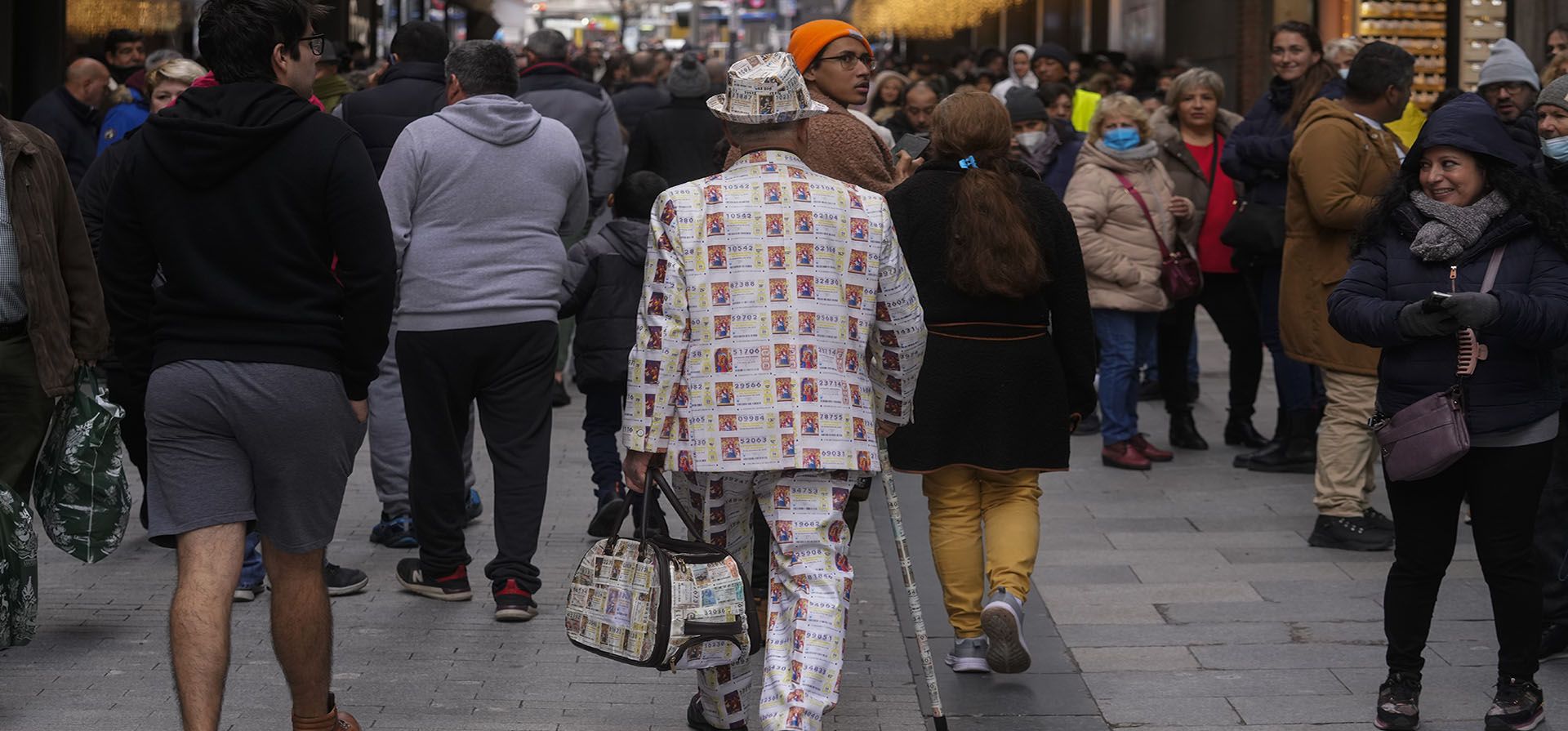 Un hombre con un traje decorado con billetes de lotería impresos camina en el centro de Madrid, España, el miércoles 21 de diciembre de 2022. La gente está comprando billetes de lotería de Navidad de última hora para el sorteo de lotería de Navidad de España conocido como El Gordo, que se llevará a cabo el 22 de diciembre. (AP Photo/Paul White)