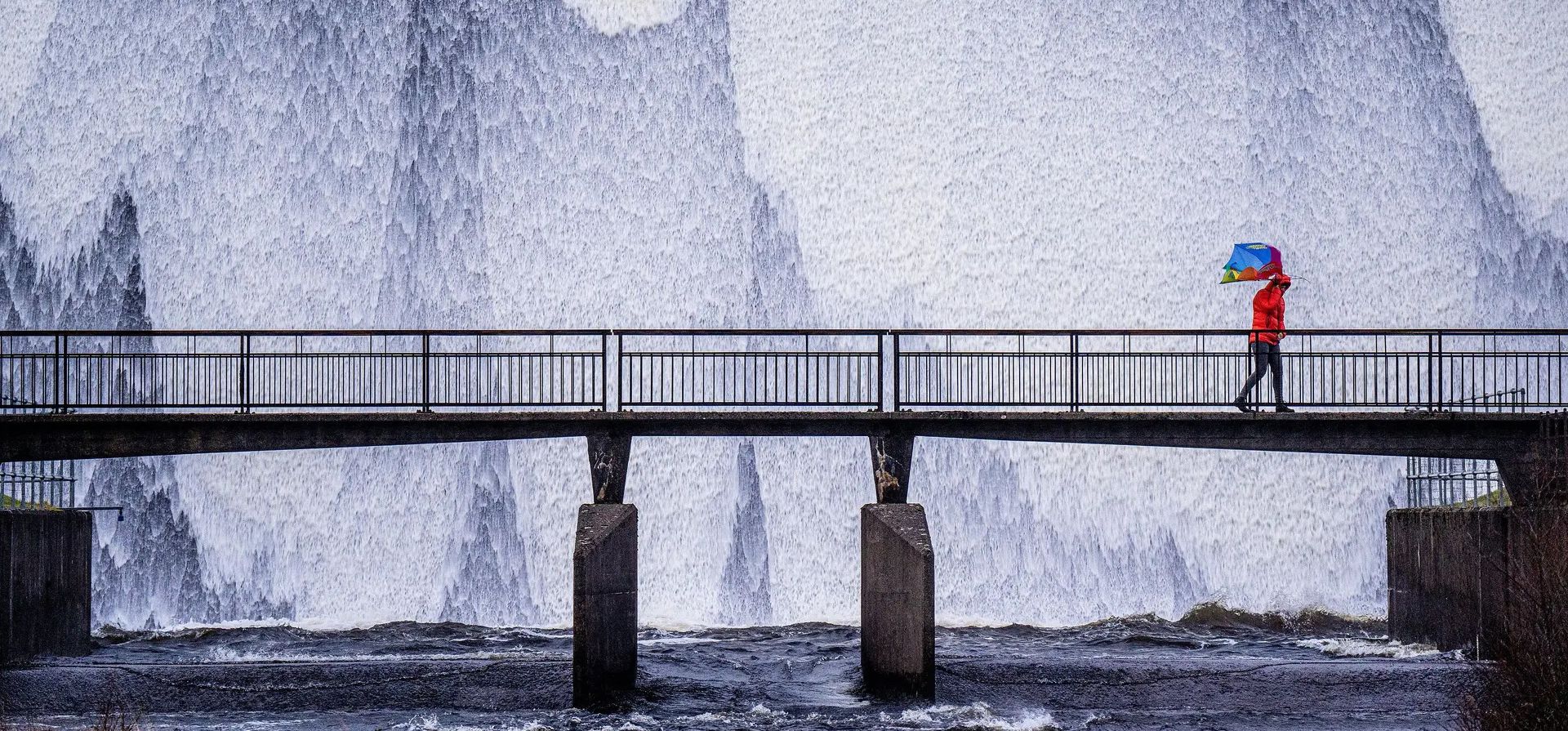 El paraguas de un transeunte se da vuelta al revés por los fuertes vientos que azota la región de Cumbria, Reino Unido, cuando cruza el puente en el embalse Wet Sleddale.
