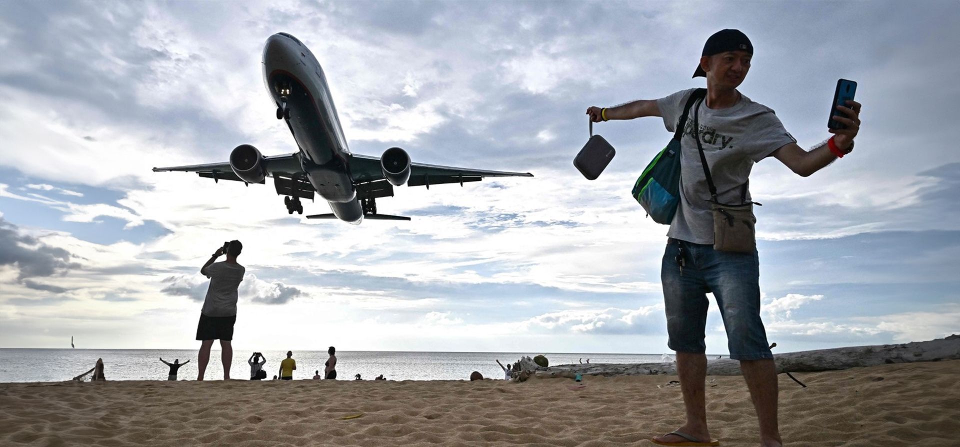 Un turista se toma una selfie en la playa de Mai Khao mientras un avión aterriza en el Aeropuerto Internacional de la isla de Phuket, Tailandia. Camboya, Tailandia y Vietnam están construyendo nuevos aeropuertos y terminales, y el próximo año se lanzará una nueva aerolínea. Foto de Lillian SUWANRUMPHA / AFP