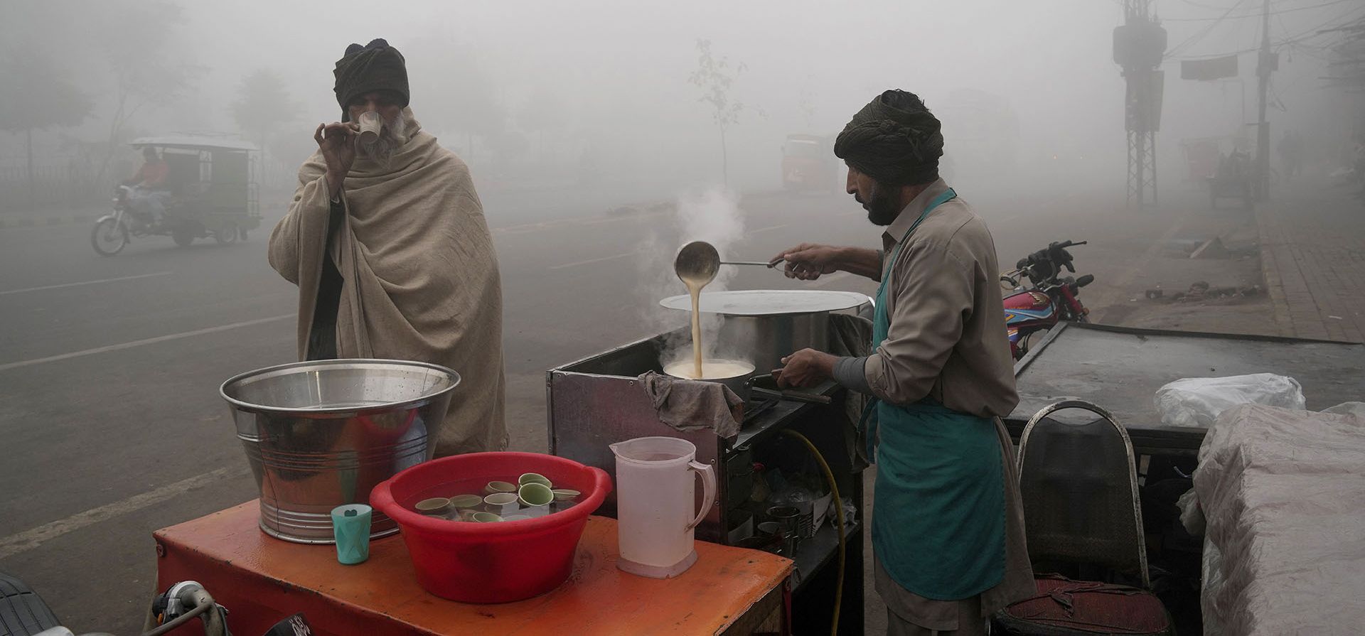 Un hombre bebe té en un puesto al borde de la carretera mientras la densa niebla reduce la visibilidad en Lahore, Pakistán, el viernes 3 de febrero de 2023. (Foto AP/K.M. Chaudary)