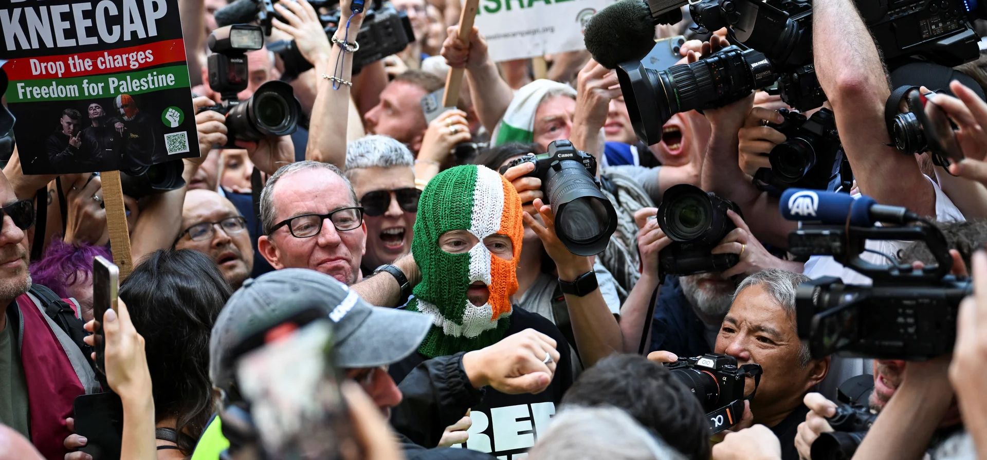 DJ Próvaí, en el centro, miembro del grupo de hip-hop Kneecap, llega al tribunal de magistrados de Westminster el día en que su compañero de banda Liam Óg Ó hAnnaidh, más conocido como Mo Chara, comparece ante el tribunal por un cargo de terrorismo en relación con la supuesta exhibición de una bandera de Hezbollah en el escenario en 2024, Londres, Reino Unido. Fotografía: Chris J Ratcliffe/Reuters DJ Próvaí, en el centro, miembro del grupo de hip-hop Kneecap, llega al tribunal de magistrados de Westminster el día en que su compañero de banda Liam Óg Ó hAnnaidh, más conocido como Mo Chara, comparece ante el tribunal por un cargo de terrorismo en relación con la supuesta exhibición de una bandera de Hezbollah en el escenario en 2024, Londres, Reino Unido. Fotografía: Chris J Ratcliffe/Reuters