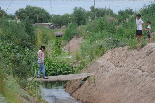 Camino. Para poder volver a su vivienda la vecina debe circular por la precaria pasarela. Los chicos observan mientras juegan sobre el montículo de tierra.