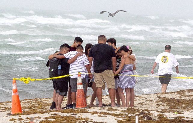 Un grupo de amigos y familiares se da consuelo en la playa, frente a los escombros del edificio destruido. Todavía hay 158 desaparecidos.