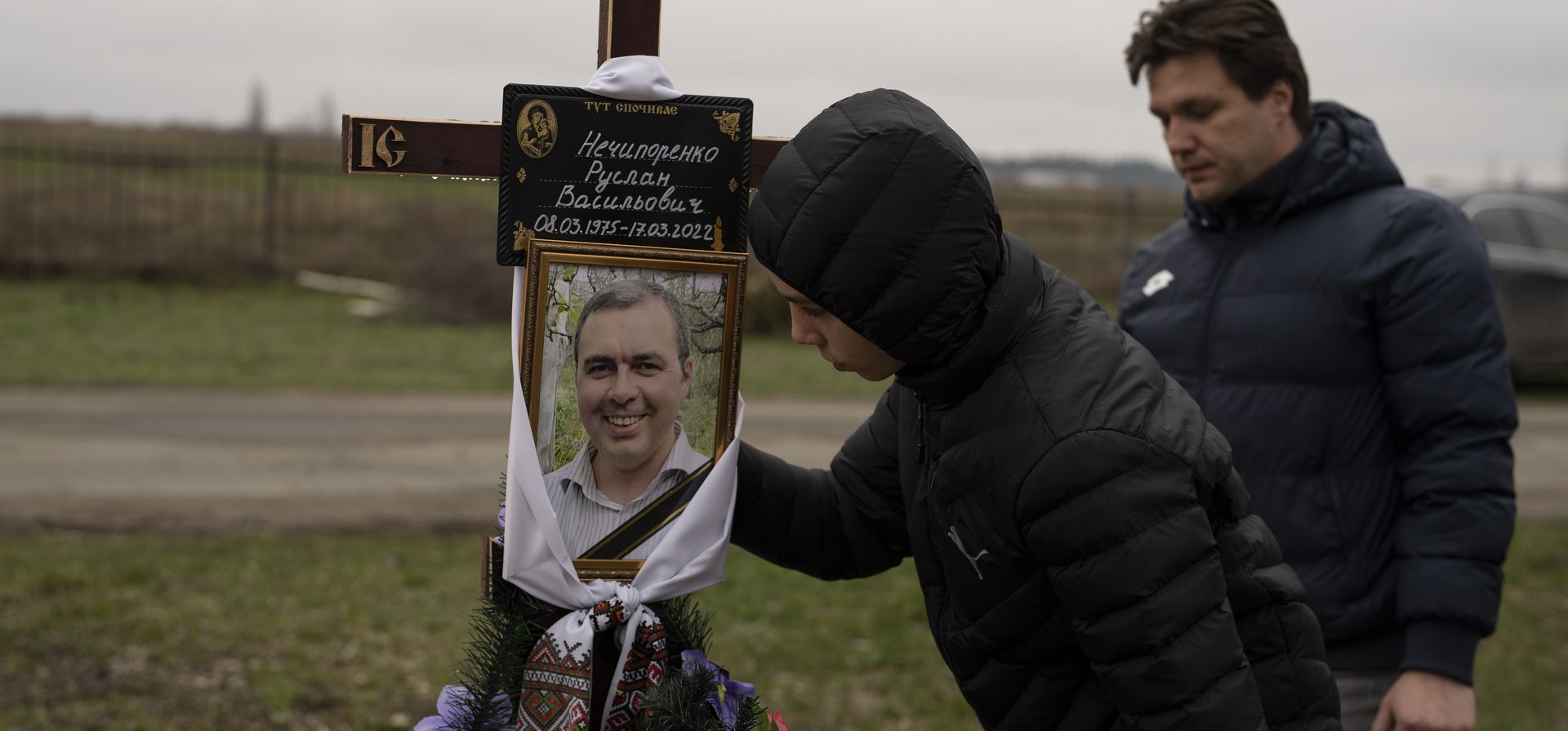 Yura Nechyporenko, de 15 años, besa las fotos de su padre Ruslan Nechyporenko frente a su tío Andriy Nechyporenko, en el cementerio de Bucha, en las afueras de Kiev, Ucrania, el jueves 21 de abril de 2022. El adolescente sobrevivió a un intento de asesinato por soldados rusos mientras su padre no tuvo la misma suerte y fue asesinado.