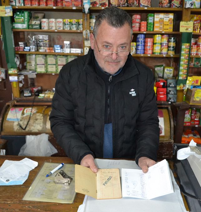 En su mano derecha, Mario Salim sostiene una libreta de fiado de la década de 1940. En la otra, una libreta actual. (Foto Corresponsalía Venado Tuerto)