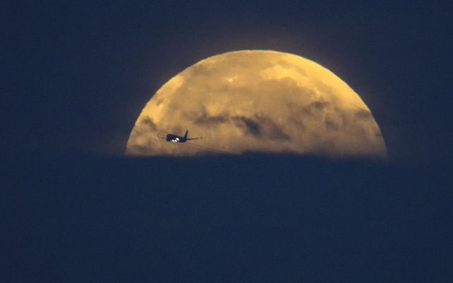 Un avión pasa volando mientras la luna llena se pone sobre la playa de Santa Mónica en California