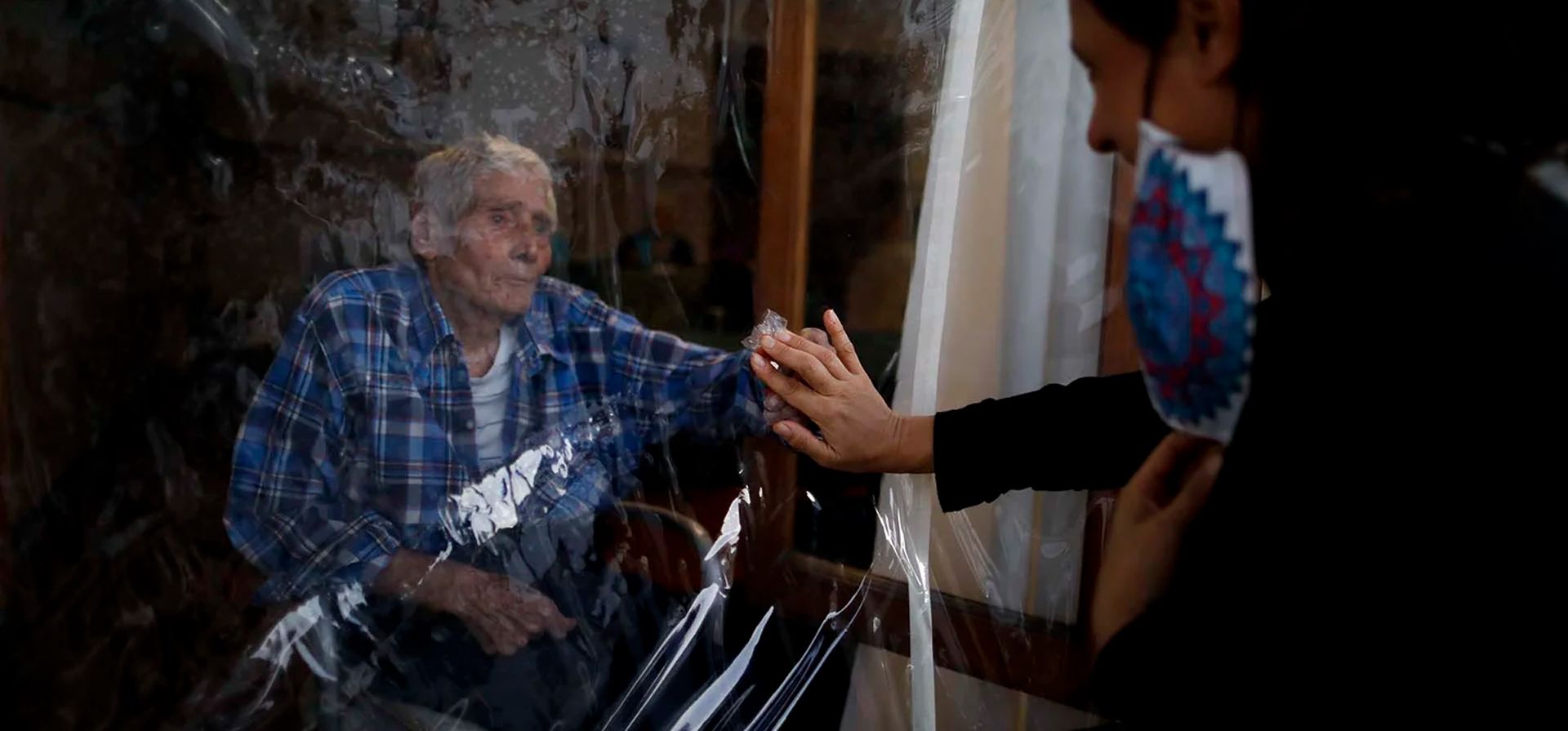 Un abuelo extiende la mano para tocar la mano de su hija, separada por una lámina de plástico para evitar la propagación del COVID-19, en la residencia de ancianos Reminiscencias en Tandil, Argentina, el 4 de abril de 2021. Foto: AP