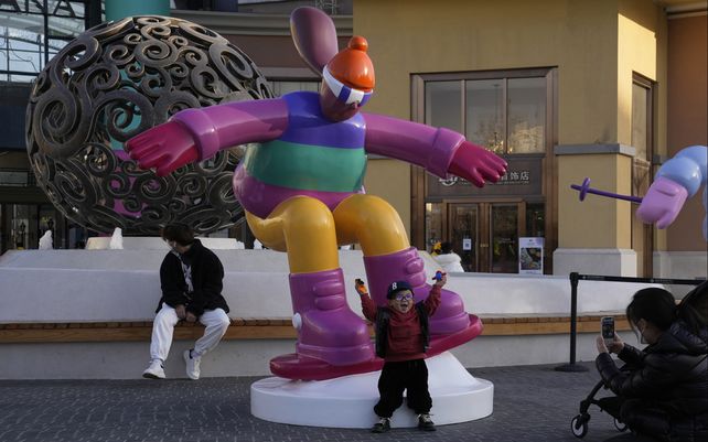 Un niño posa para las fotos cerca de una escultura que representa deportes de invierno en Beijing