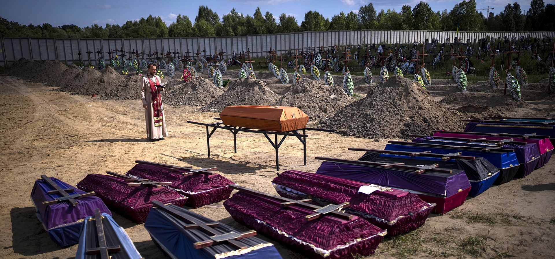 Un sacerdote bendice ataúdes con cuerpos civiles no identificados, que murieron en el territorio de la comunidad de Bucha durante el período de ocupación rusa en febrero-marzo de 2022, durante un funeral en Bucha, cerca de Kyiv, Ucrania, el viernes 2 de septiembre de 2022.