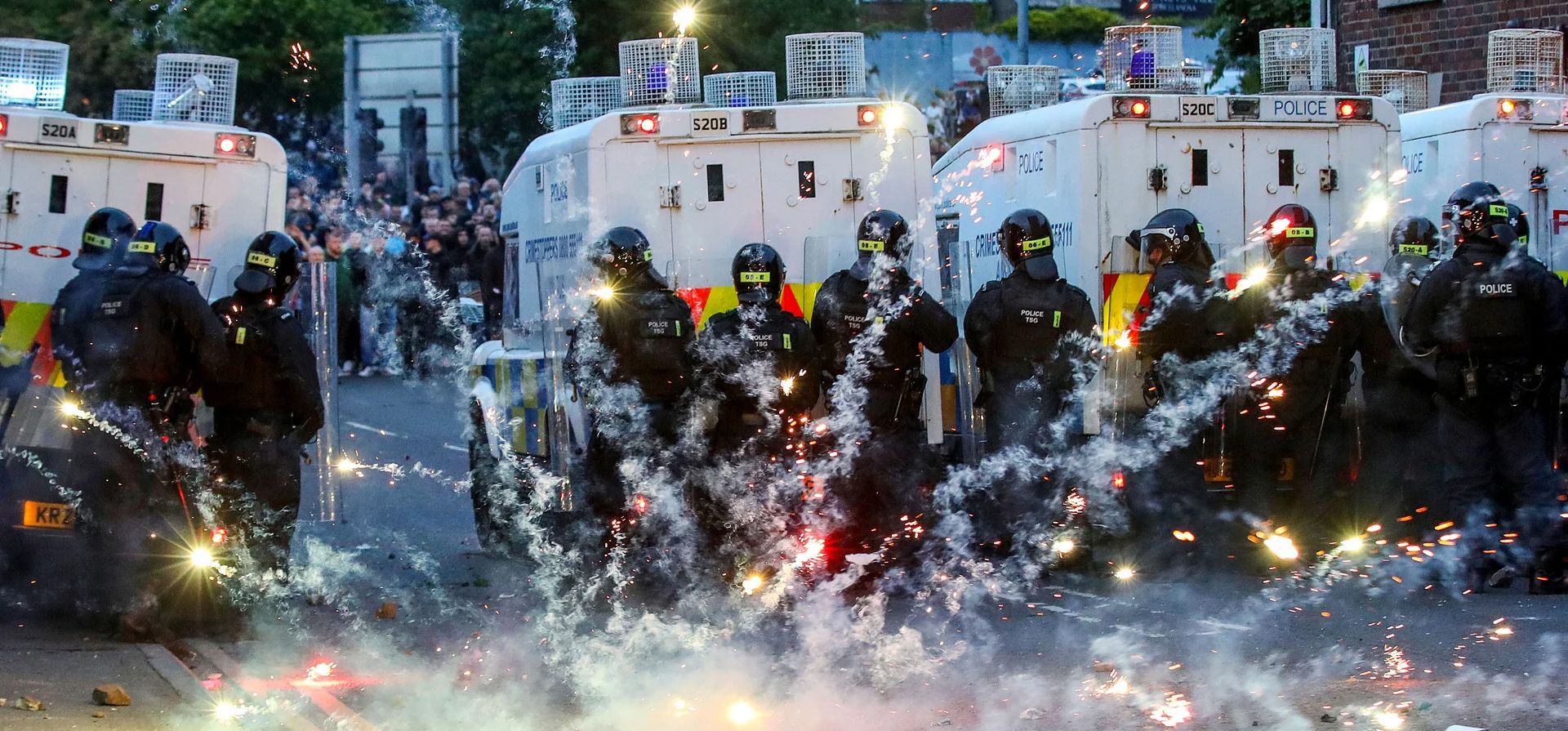Petardos lanzados por manifestantes antiinmigración explotan frente a la policía antidisturbios, Ballymena, Irlanda del Norte. Fotografía: Paul Faith/AFP/Getty Petardos lanzados por manifestantes antiinmigración explotan frente a la policía antidisturbios, Ballymena, Irlanda del Norte. Fotografía: Paul Faith/AFP/Getty