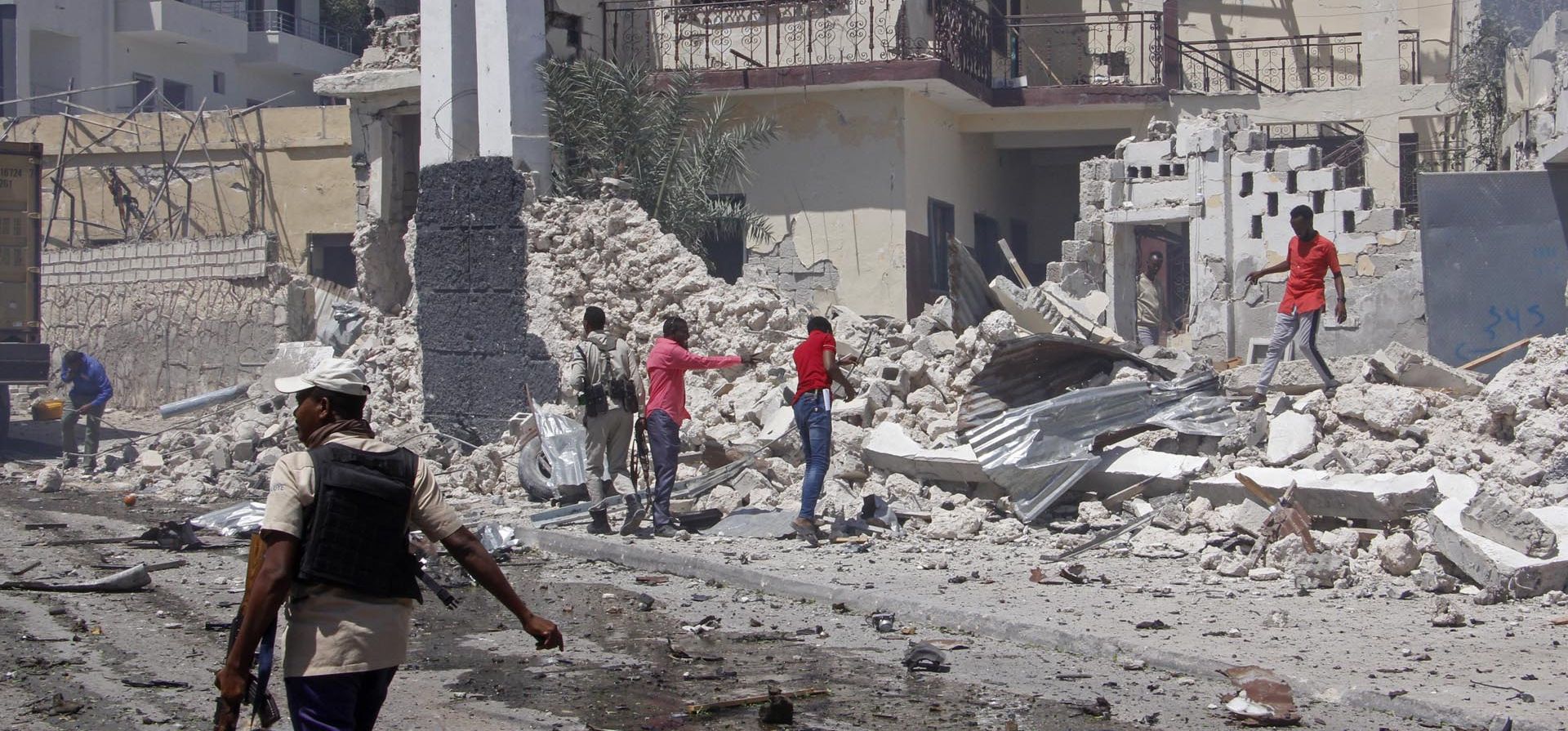Rescatistas y fuerzas de seguridad revisan los restos en el lugar de una explosión en Mogadishu, Somalia el miércoles 12 de enero de 2022. El miércoles se informó de una gran explosión fuera del aeropuerto internacional de la capital de Somalia y un socorrista dijo que hubo muertos y heridos.
