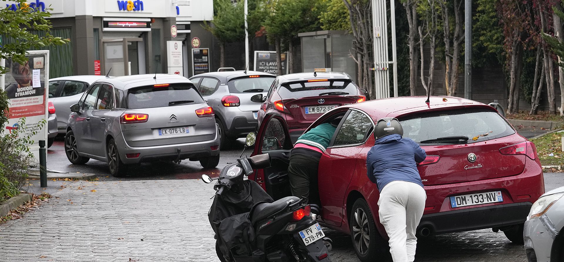 Un conductor de scooter ayuda a un automovilista que empuja su automóvil para llegar a una estación de servicio, el viernes 14 de octubre de 2022, en Nanterre, en las afueras de París. Las huelgas en las refinerías francesas interrumpió gravemente el suministro de combustible cuando el sindicato de extrema izquierda CGT rechazó un acuerdo sobre el aumento salarial que se encontró entre el gigante de la energía y otros dos sindicatos más moderados.