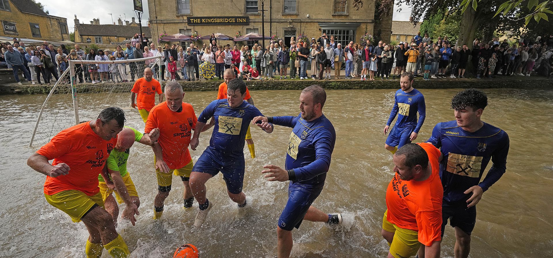 Futbolistas de Bourton Rovers disputan el balón durante el tradicional partido de fútbol anual River Windrush, que se lleva a cabo durante más de 100 años, en el pueblo de Bourton-on-the-Water, Inglaterra, en los Cotswolds, el lunes 28 de agosto de 2023. (Ben Birchall/PA vía AP) Futbolistas de Bourton Rovers disputan el balón durante el tradicional partido de fútbol anual River Windrush, que se lleva a cabo durante más de 100 años, en el pueblo de Bourton-on-the-Water, Inglaterra, en los Cotswolds, el lunes 28 de agosto de 2023. (Ben Birchall/PA vía AP)