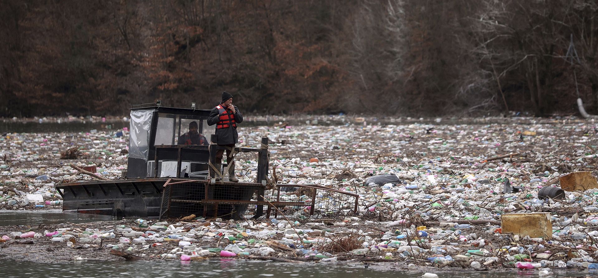 Trabajadores de una empresa de servicios públicos empujan los desechos a la orilla del río Lim cerca de Priboj, Serbia, el lunes 30 de enero de 2023. Botellas de plástico, tablones de madera, barriles oxidados, detrás de una barrera de basura en el río Lim en el suroeste de Serbia. (Foto AP/Armin Durgut)