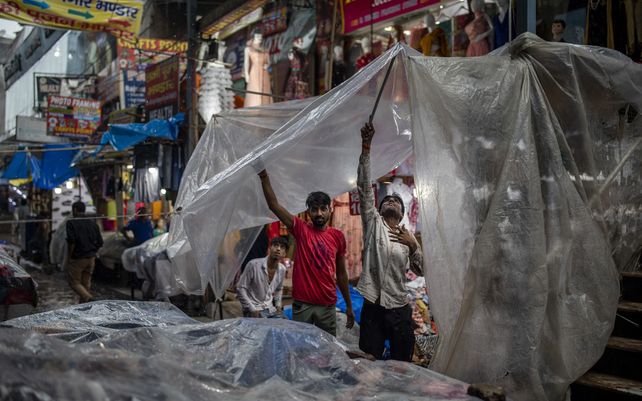 Vendedores ambulantes cubren sus puestos con polietileno mientras llueve en Noida