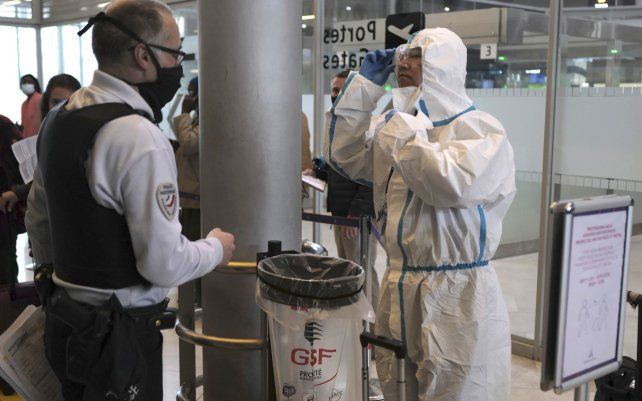 Un pasajero de Taiwán con equipo de protección es registrado por un oficial de policía francés antes de abordar un avión en el aeropuerto Charles de Gaulle de París en Roissy, al norte de París.