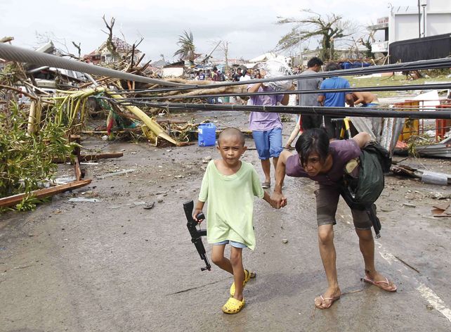 Una mujer y su hijo pasan por debajo de los cables de electricidad derribados por el tifón en la ciudad de Tacloban