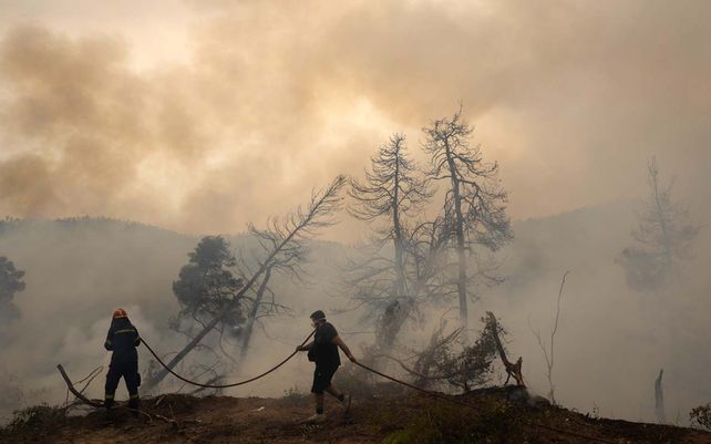 Un bombero intenta apagar las llamas mientras un residente local sostiene una manguera de agua durante un incendio forestal en la aldea de Ellinika en la isla de Evia