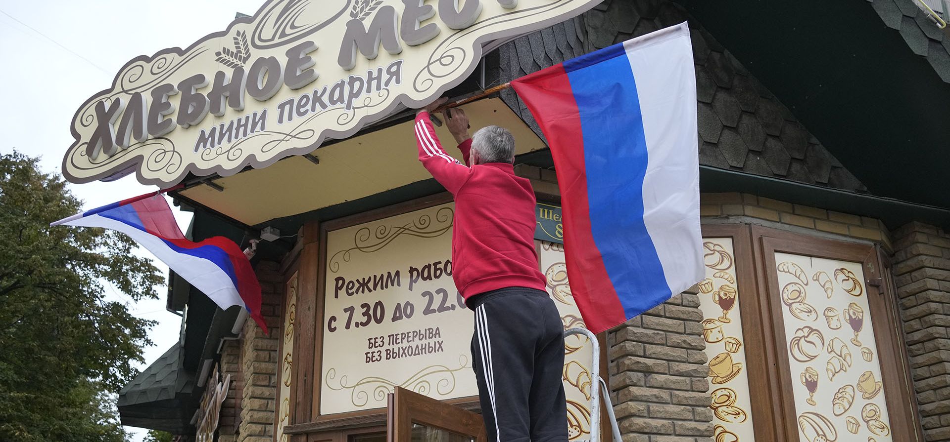 Un hombre cuelga una bandera rusa en un café en Lugansk, República Popular de Luhansk controlada por separatistas respaldados por Rusia, este de Ucrania, el martes 27 de septiembre de 2022}. La votación comenzó el viernes en cuatro regiones de Ucrania controladas por Moscú sobre referéndums para convertirse en parte de Rusia.